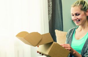 A female online shopper smiles as she opens a parcel delivery.