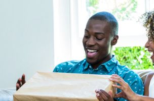 man in a blue shirt smiling animatedly, holding a large brown parcel