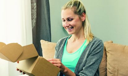 A female online shopper smiles as she opens a parcel delivery.